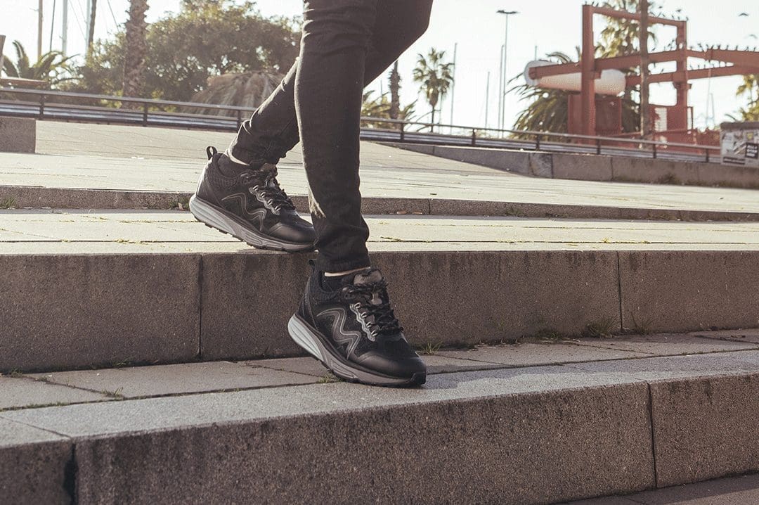 Nærbillede af dame i sorte MBT Tevo Black sneakers på en trappe udendørs.